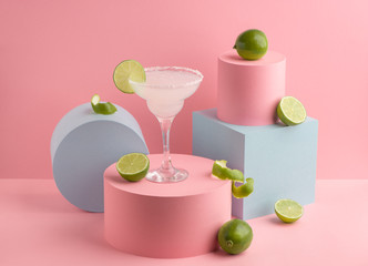 Glass of Margarita cocktail and fresh limes on pink background