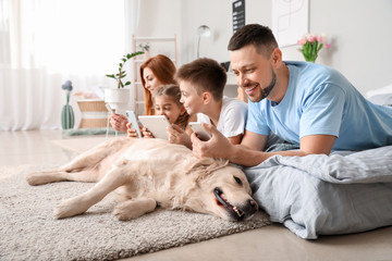 Happy family with modern devices and dog in bedroom at home