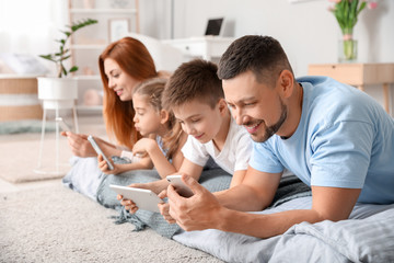 Happy family with modern devices in bedroom at home