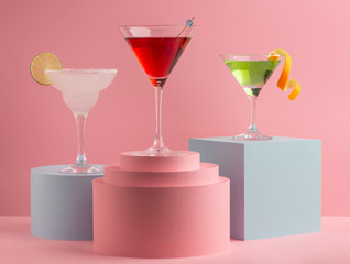 Glasses of different cocktails on pink background