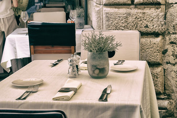Table setting on summer terrace of cozy restaurant. Vase with flowers, plates, cutlery and tablecloth for a festive dinner. Decorated holiday table.