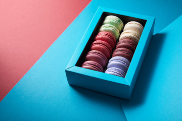 assorted delicious bitten colorful french macaroons in box on blue and red background