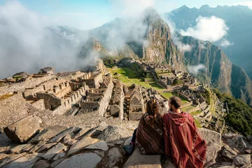 Foto auf Acrylglas Machu Picchu Ein Paar in Ponchos gekleidet, das die Ruinen von Machu Picchu beobachtet
