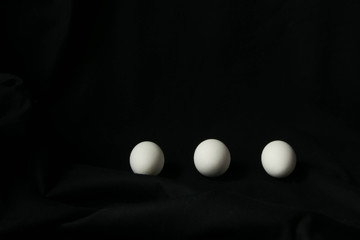 three white chicken eggs on a black background