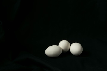 three white chicken eggs on a black background