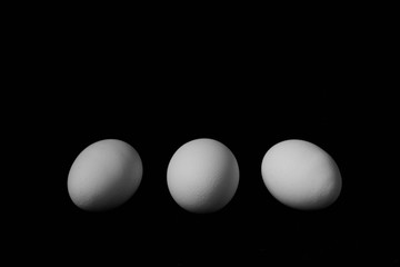 three white chicken eggs on a black background