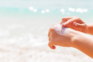 Woman in swimwear is applying sun cream on her hand with her finger at the sea background