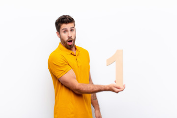 young handsome man surprised, shocked, amazed, holding a number 1.