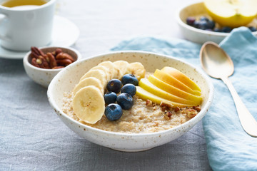 Whole oatmeal, large bowl of porridge with banana, blueberries, apple, nuts. Side view, close up