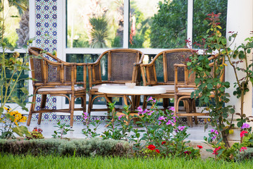 Wicker, wooden furniture, table and chairs on the summer terrace surrounded by southern plants