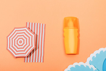 Top view of dispenser bottle of sunscreen with paper cut sea waves on orange background