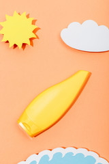 Top view of paper cut sun, cloud and sea wave with tube of sunscreen on orange