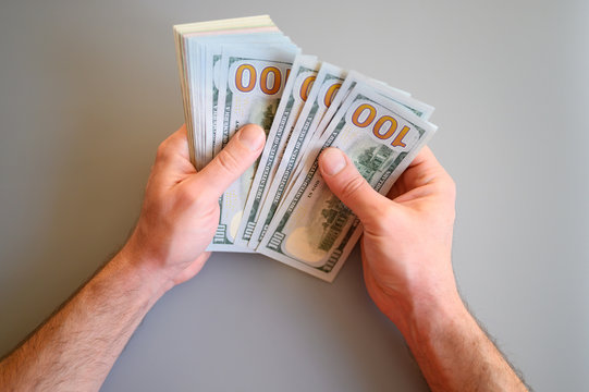 men's hands hold and count 100 dollar bills on gray background
