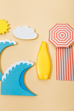 Top view of paper cut beach with yellow tube of sunscreen on beige