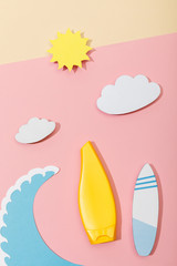 Top view of paper cut summer beach with tube of sunscreen on pink and beige