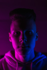 Young guy in a neon light. A teenager in a pink hoodie in trendy lighting of pink, purple and blue