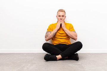 young blonde man happy and excited, surprised and amazed covering mouth with hands, giggling with a...