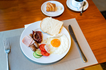 Fresh breakfast table next to window with bread, pastry, egg, fruit, juice, coffee cup