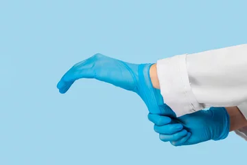 Foto op Plexiglas The doctor puts on sterile gloves on a blue background. Infection control concept. Danger of spread of infection © Nana_studio