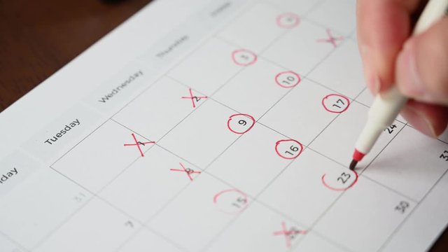 The hand of a man holding a pen in his hand and recording his schedule on a desk calendar.
