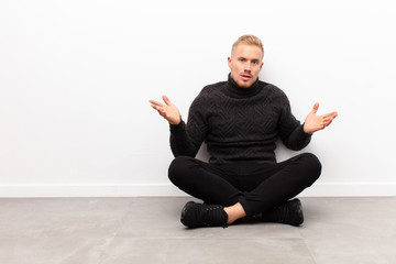 young blonde man feeling puzzled and confused, unsure about the correct answer or decision, trying...