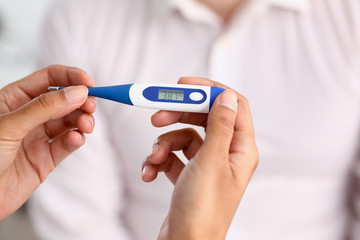 hands of a female doctor holding a thermometer with a patient's high temperature in hand