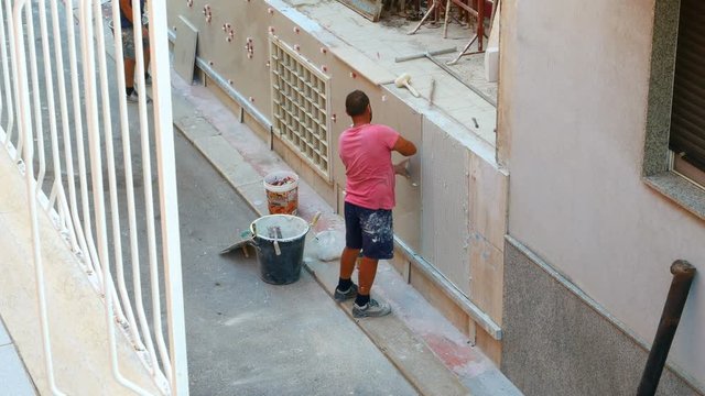 Worker labor building wall and UPVC groove line with plaster cement at house construction site
