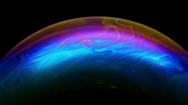 Close-up of soap bubble. Multicolored rainbow iris like colorful gas planet on black background. Abstract multi-colored surface overflows with abstract patterns