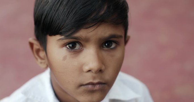 Extreme closeup of a good looking sweet Indian boy looking at camera with his beautiful eyes and smiles, CU looking up down bokeh separation out of focus background red pink porch house confident shy