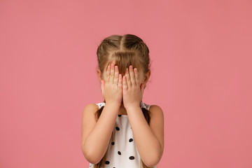 Cute little child girl closes her eyes with her hand on pink background. I see nothing