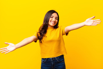 young latin pretty woman smiling cheerfully giving a warm, friendly, loving welcome hug, feeling happy and adorable against flat wall