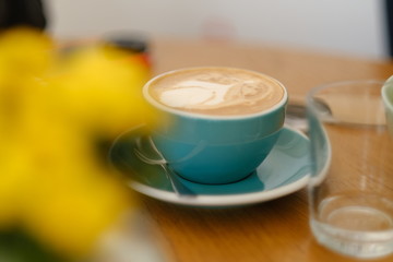 Breakfast in the cafe. Beautiful blue mug with cappuccino or latte coffee on a wooden table. View from above. 