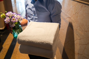 Closeup Asian hotel chambermaid man holding clean folded towels in hotel corridor