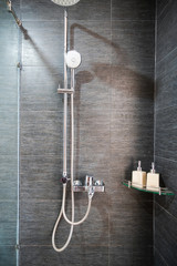 Hotel bathroom closeup with stainless hanging shower, bottles of shower and shampoo gel