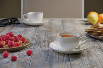 Morning tea for breakfast: puff pastry with and jam, raspberry, with various fruit on the background.  Сhocolate candy, sunglasses, brown-gray wooden table