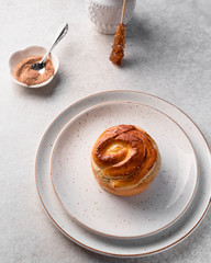 a muffin on a light ceramic plate, cinnamon, sugar cone, on a light marble table, a dessert