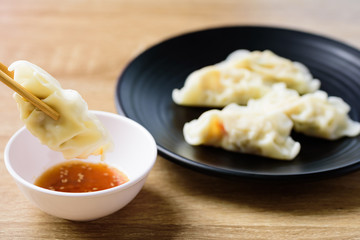 Steamed wonton dumpling stuffed with minced pork and shrimp eating with sesame oil sauce by using chopsticks, Asian food