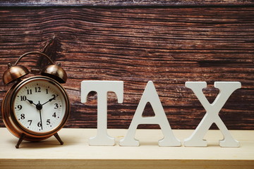 Alarm clock and Tax alphabet letter on wooden background