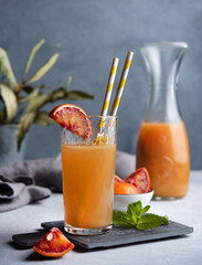sweet freshly squeezed  orange juice with a slice of red orange and mint on a gray-blue background