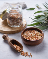 green vegan buckwheat in a wooden bowl , spoon and glass jar on a light grey background