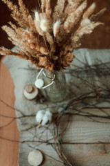  Still life of creating a spring wreath of branches, dried flowers on a wooden table. Nearby are vases with ears of corn. room, window. Flat lay.