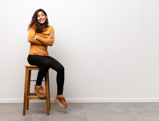 young pretty woman feeling happy, shocked and surprised, covering mouth with hand and pointing to lateral copy space sitting into a room © kues1