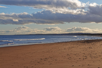 St Cyrus beach with the tide out, looking towards Montrose and Scurdie Ness Lighthouse on a golden February evening.