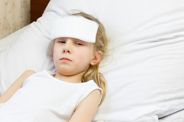 A girl with white hair lies in bed. She has a bandage on her forehead to relieve pain. Close-up. There is a tint