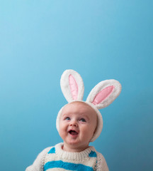 Cute little baby wearing white easter bunny ears against a blue background