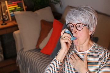 Senior woman using asthma inhaler at home 