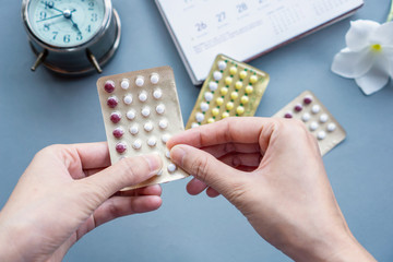 woman hand taking oral contraceptive pills, with calendar and clock on background 