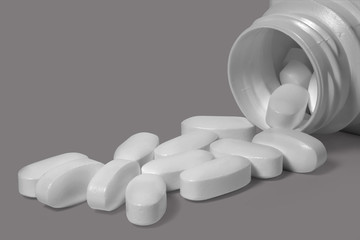 Overturned jar with oval pills on a gray background