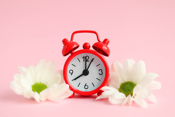Concept of early spring, red alarm clock with flowers on a pink background