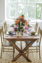 Boho chic style. Decorated wooden table with ceramic plates, cutlery, glasses for drinks, a vase with fresh flowers and candles. Golden chairs. Peonies, Succulents, orchids and Leucospermum.